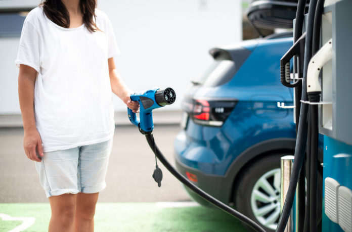 Woman charge Electric car on gas station. Blue car and electric