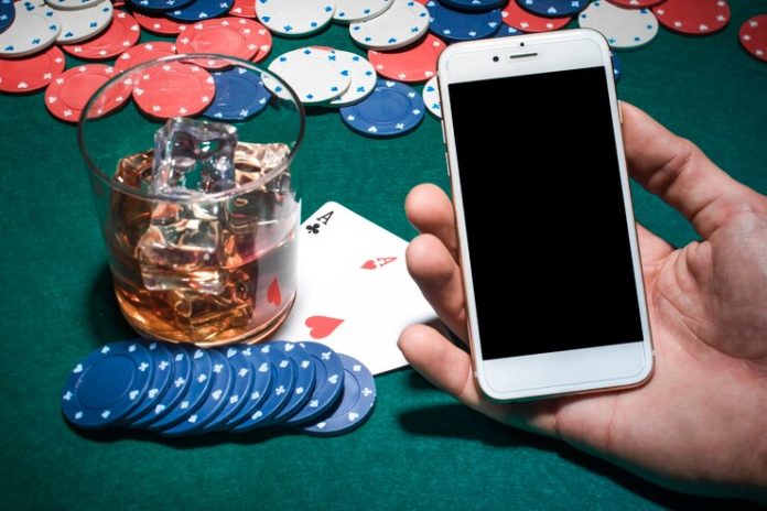mano-dell-uomo-che-tiene-cellulare-sopra-il-tavolo-da-poker-con-bicchiere-di-whisky_23-2147881019